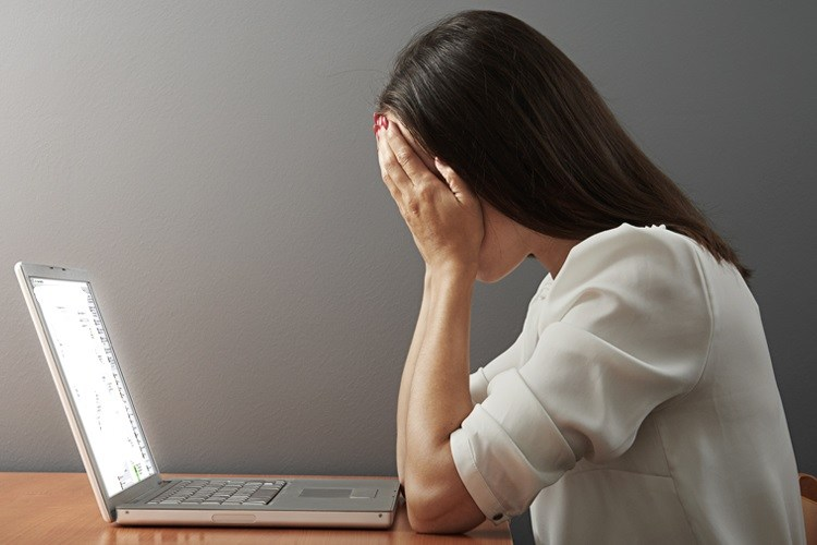 femme assise devant un ordinateur portable, paume sur le visage