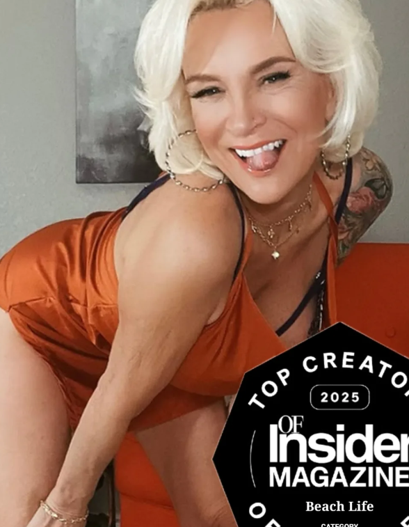 Ageless Vixen in orange top bending over in seductive shot